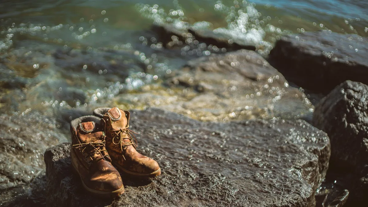 Abandoned hiking boots on a rocky shoreline with waves crashing in.