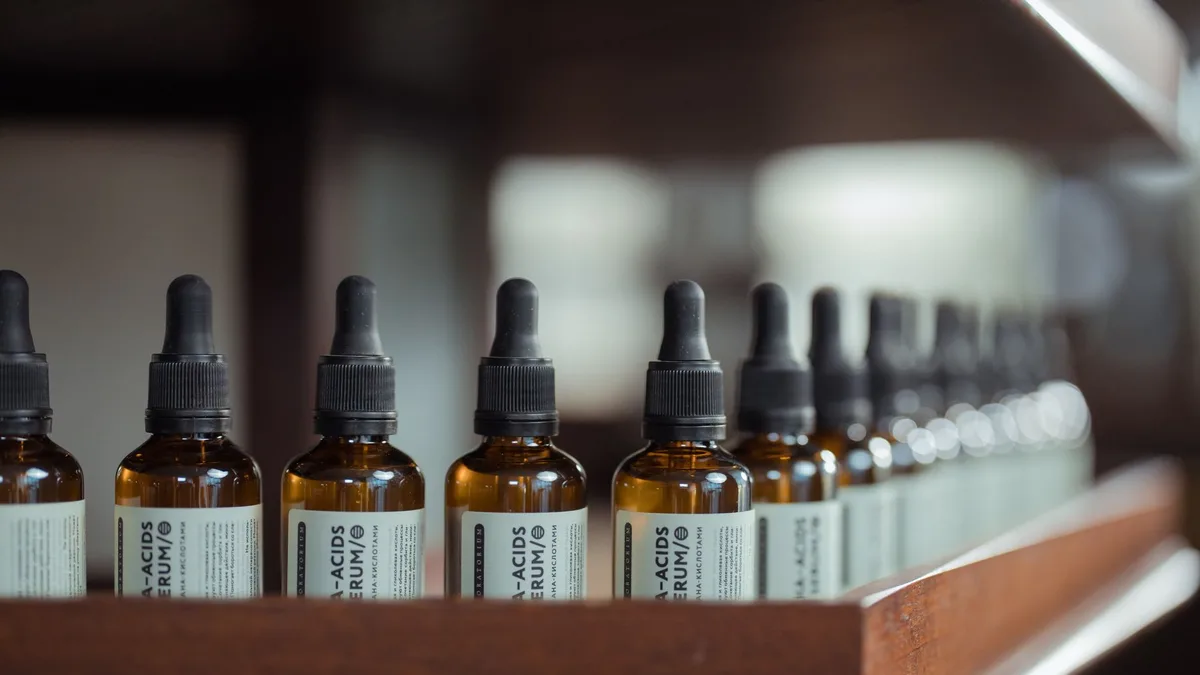 Row of brown serum bottles with dropper caps aligned on a wooden shelf.