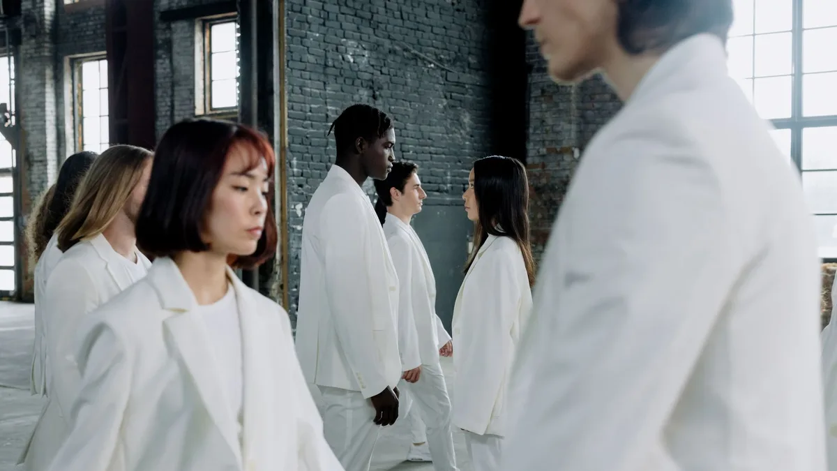 A group of diverse models in white suits walking indoors with natural light.