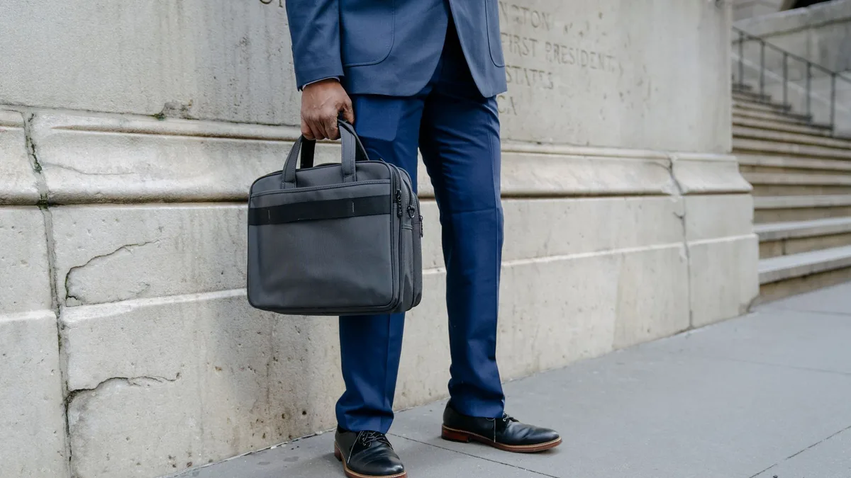 Businessman in blue suit holding a briefcase outside a stately building, urban setting.