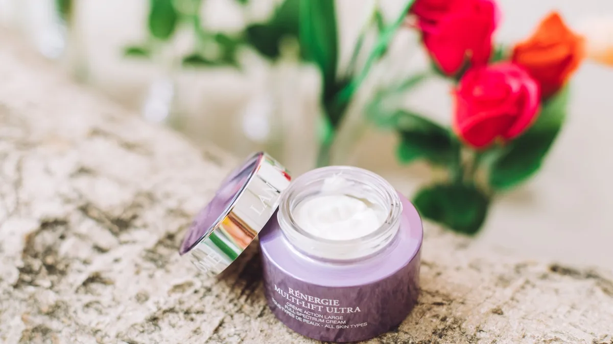 Open jar of luxury skincare cream surrounded by vibrant red roses on a textured surface.