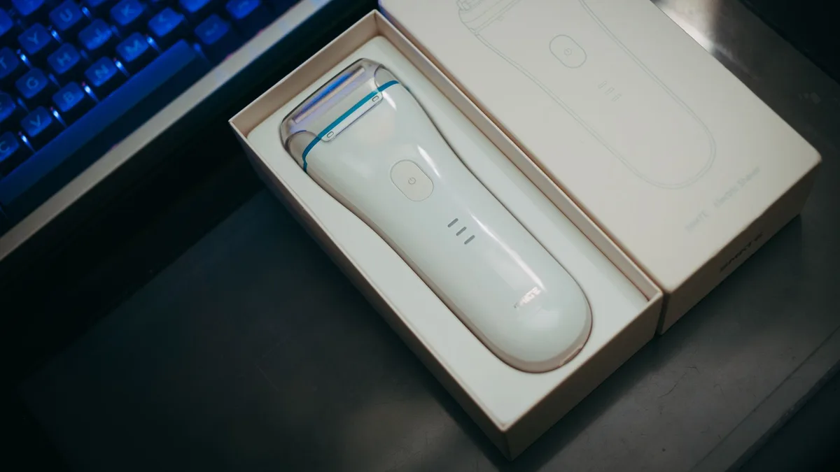 White electric shaver in elegant box beside keyboard on a dark surface.