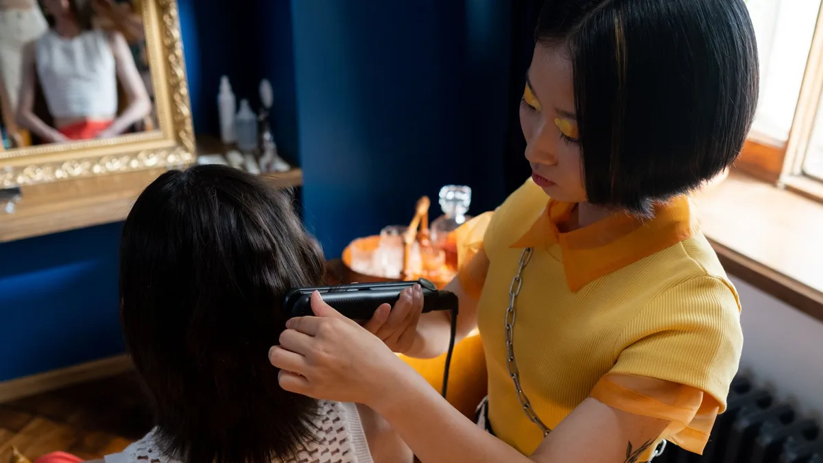 A hairdresser styles a client's hair with a straightener in a modern salon setting.