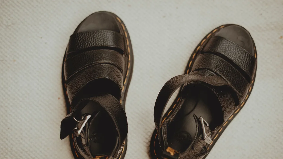 Close-up of black leather sandals with buckle straps on a textured beige surface.