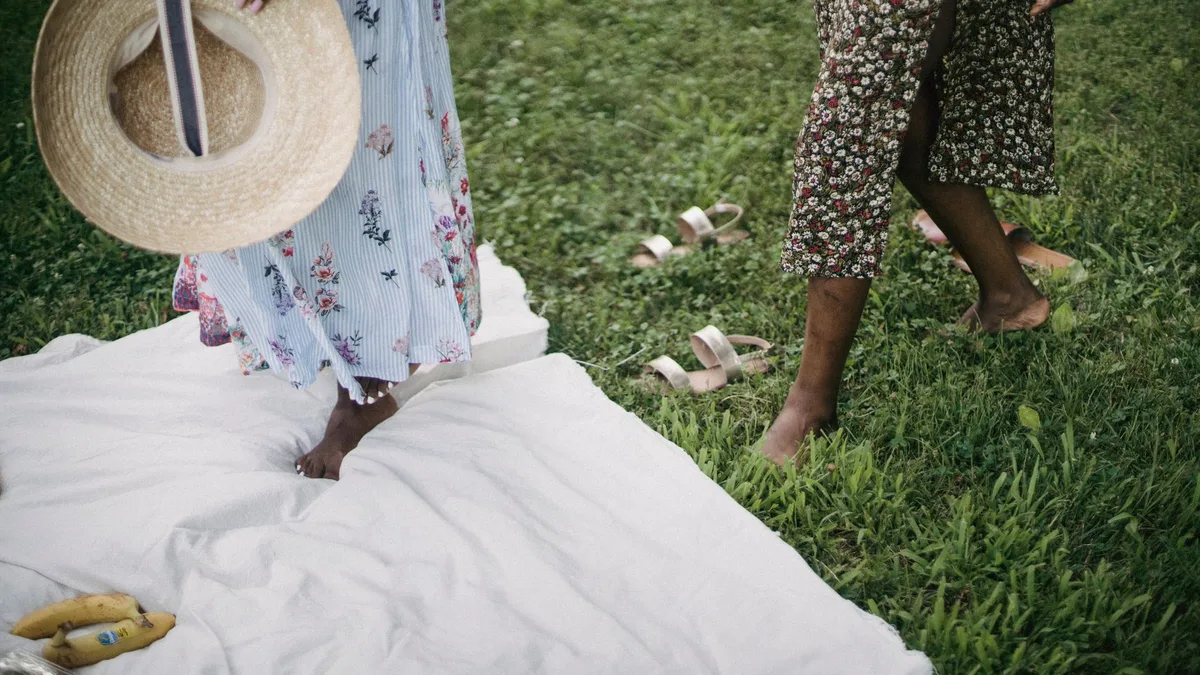 Two women enjoy a picnic outdoors, dressed in floral dresses, capturing a vibrant summer vibe.